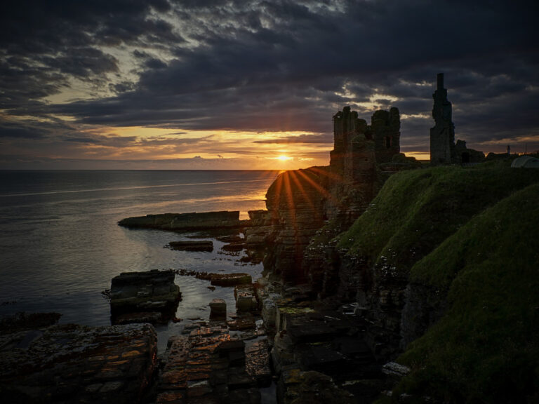 Castle Sinclair Girnigoe ruins perched on a cliff edge overlooking the rugged North Sea at sunrise on the Caithness coast in Scotland.